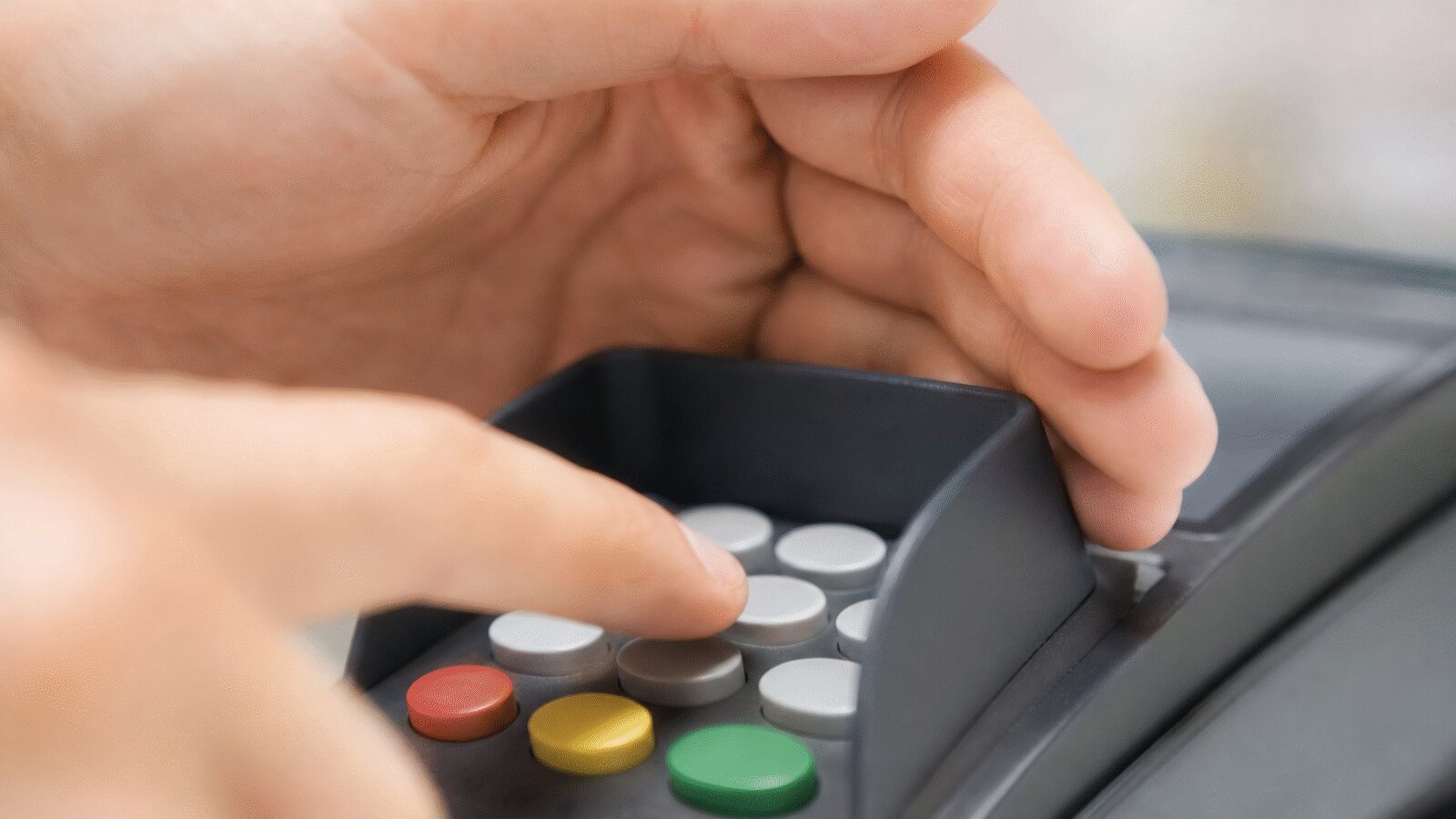 Hand covering the keypad of a payment terminal while entering a PIN